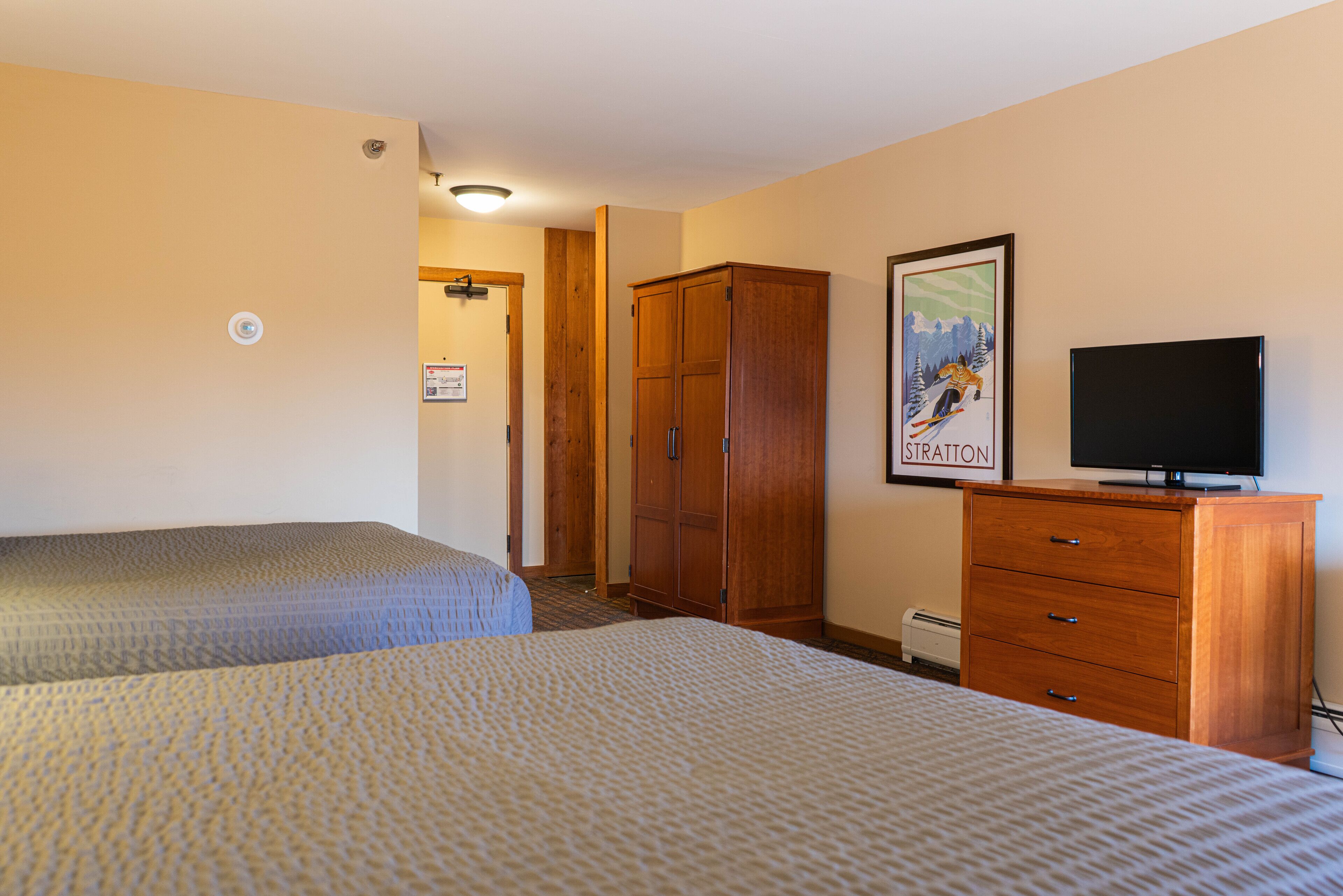 Ein Hotelzimmer mit zwei Betten, einem Holzschrank, einem Fernseher und einem Bild an der Wand.