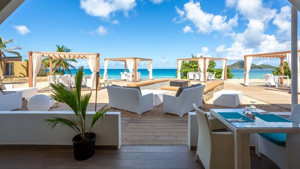 Un espace extérieur aménagé avec des meubles en osier blanc, offrant une vue sur la plage et l’océan.