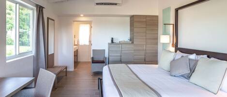 A hotel room with a bed, a desk, a chair, a ceiling fan, and a view of the outdoors.