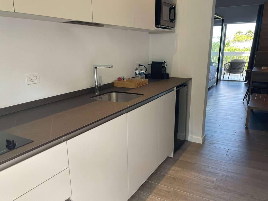 Una cocina moderna con estufa integrada, un lavamanos y un microondas. En la encimera, hay una bandeja de madera con una cafetera y una botella.