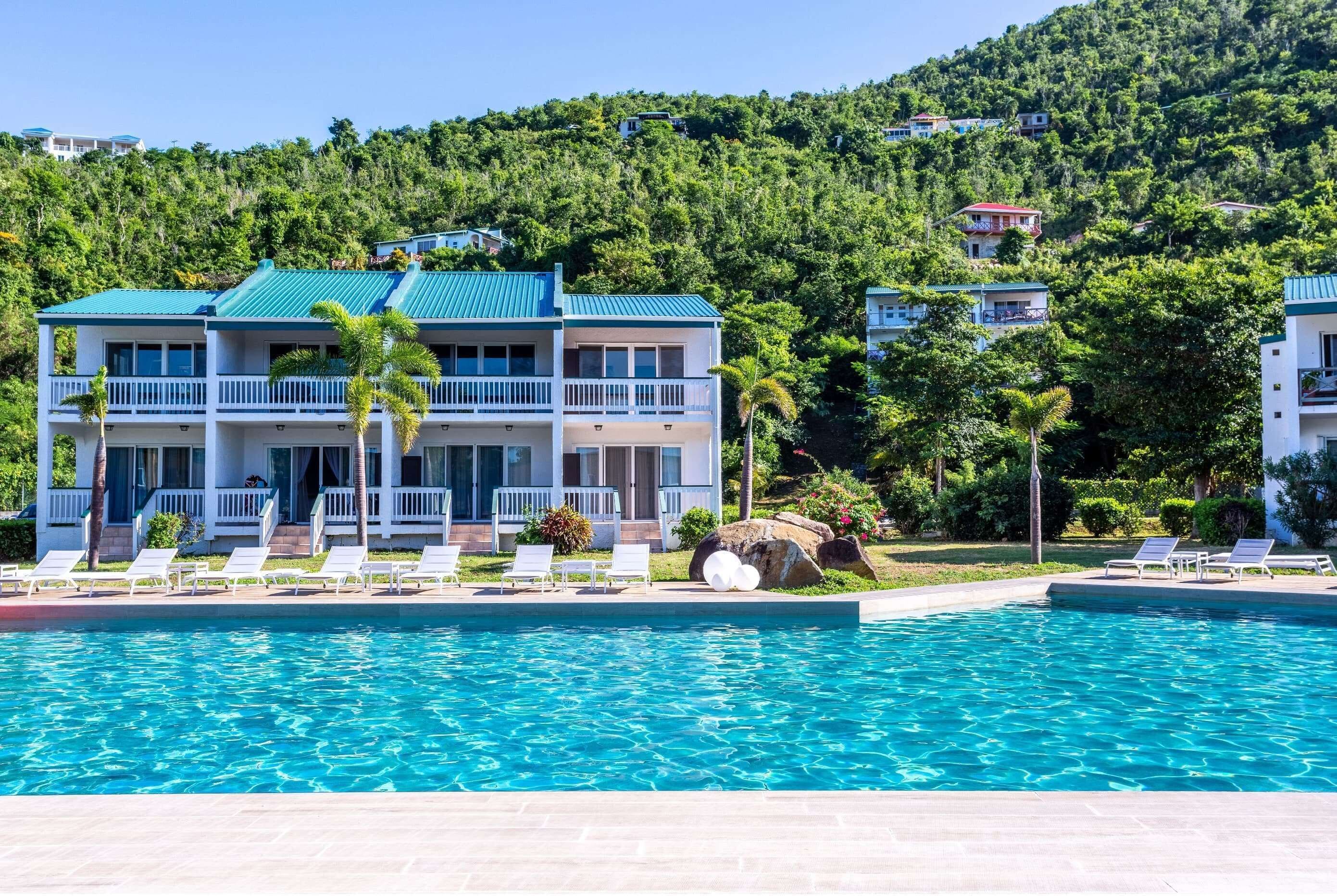 Un resort con piscina, balcones blancos y un exuberante paisaje montañoso de color verde.