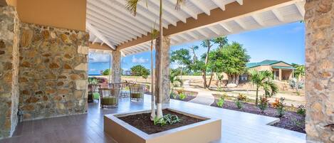 A covered outdoor area with a stone wall, a palm tree planter, and a view of a residential neighborhood.