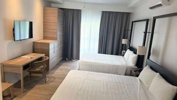 A hotel room with two beds, a desk, a chair, a TV, and a ceiling fan.