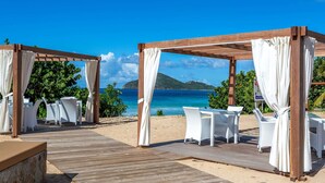 Une terrasse en bois, meublée de mobilier en osier blanc, avec vue sur l’océan.
