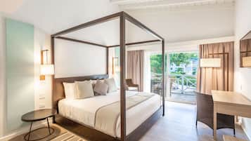 A four-poster bed with a wooden frame, a small round table, a chair, and a desk with a lamp.