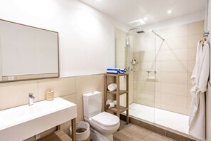 Un baño moderno con lavamanos blanco, inodoro y ducha con mampara de vidrio.