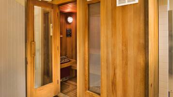 A wooden sauna room with a glass door, a visible heater, and a sign warning about overheating.