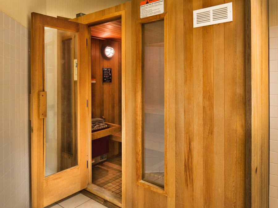 Un sauna en bois avec une porte en verre, un appareil de chauffage visible et un panneau d’avertissement concernant le risque de surchauffe.