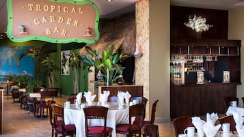Ravintola, jonka teemana on trooppinen tunnelma. Siellä on esimerkiksi kyltti, jossa lukee ”Tropical Garden Bar”, puisia pöytiä ja tuoleja sekä baaritiski, jossa on esillä pulloja ja laseja.
