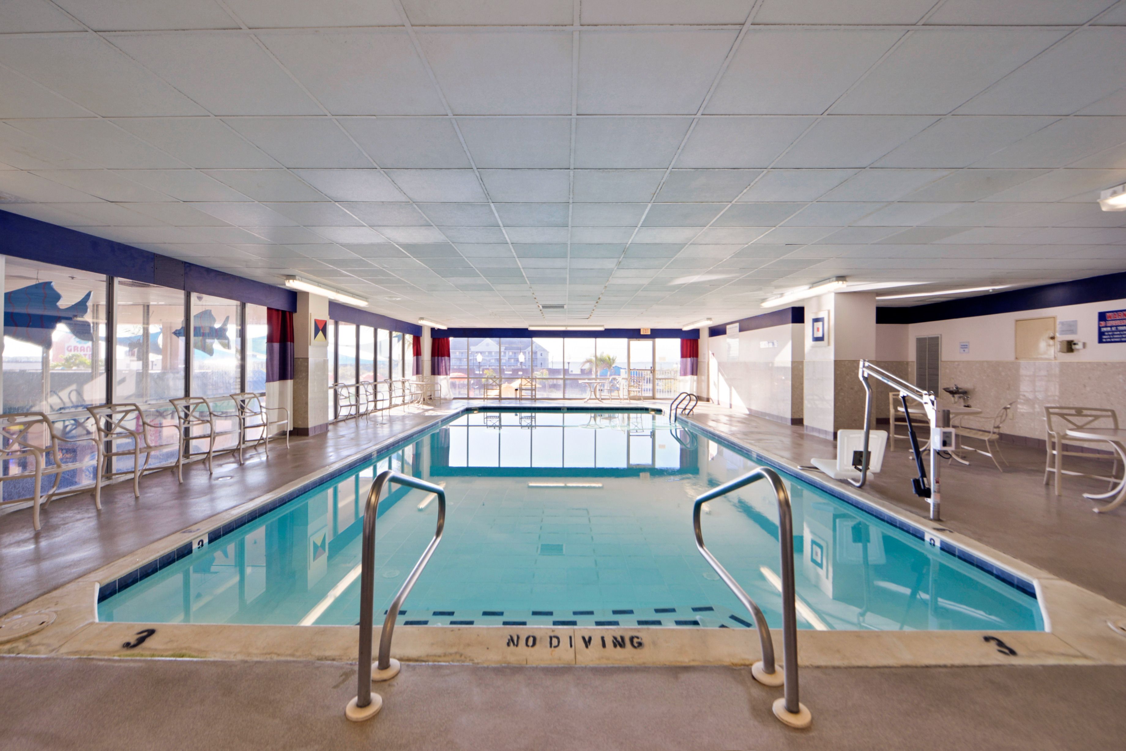 En indendørs swimmingpool med klart vand, et skilt med 'No Diving', og udsigt til det fri gennem store vinduer.