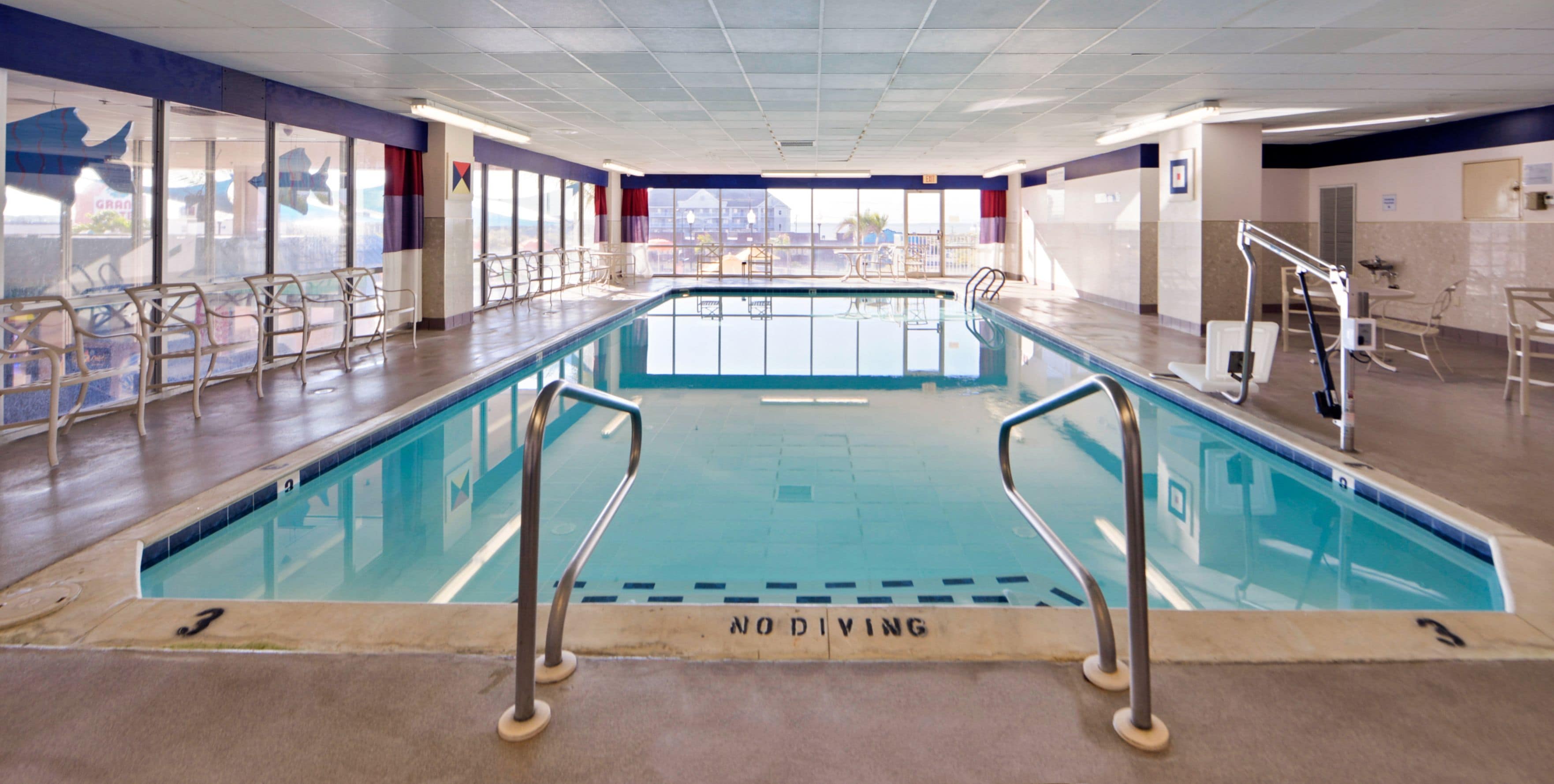Une piscine intérieure à l’eau claire, dotée de rampes en métal et d’un panneau indiquant qu’il est interdit de plonger.