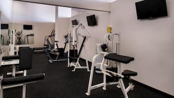 Une salle de sport équipée de divers appareils d’exercice, d’un téléviseur fixé au mur et d’un miroir qui reflète les équipements.