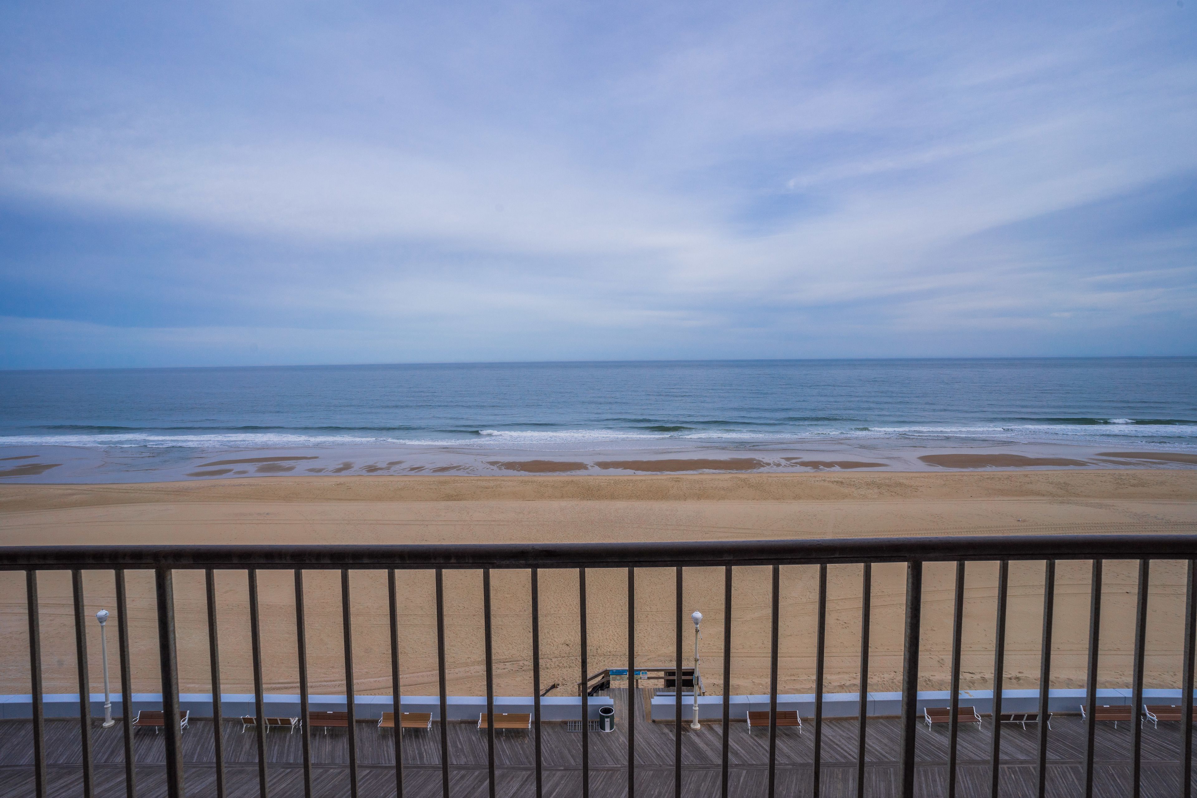 A beach view from a balcony with a railing, wooden deck, and benches.