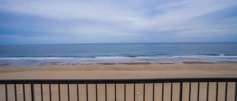 Vista a la playa desde un balcón con barandilla, terraza de madera y bancos.