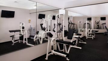 A gym with various exercise machines, a large mirror, and a television on the wall.