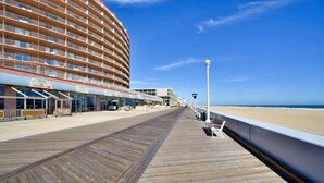 Un paseo marítimo de madera que lleva a un hotel frente a la playa, con varios balcones y una vista despejada del océano.