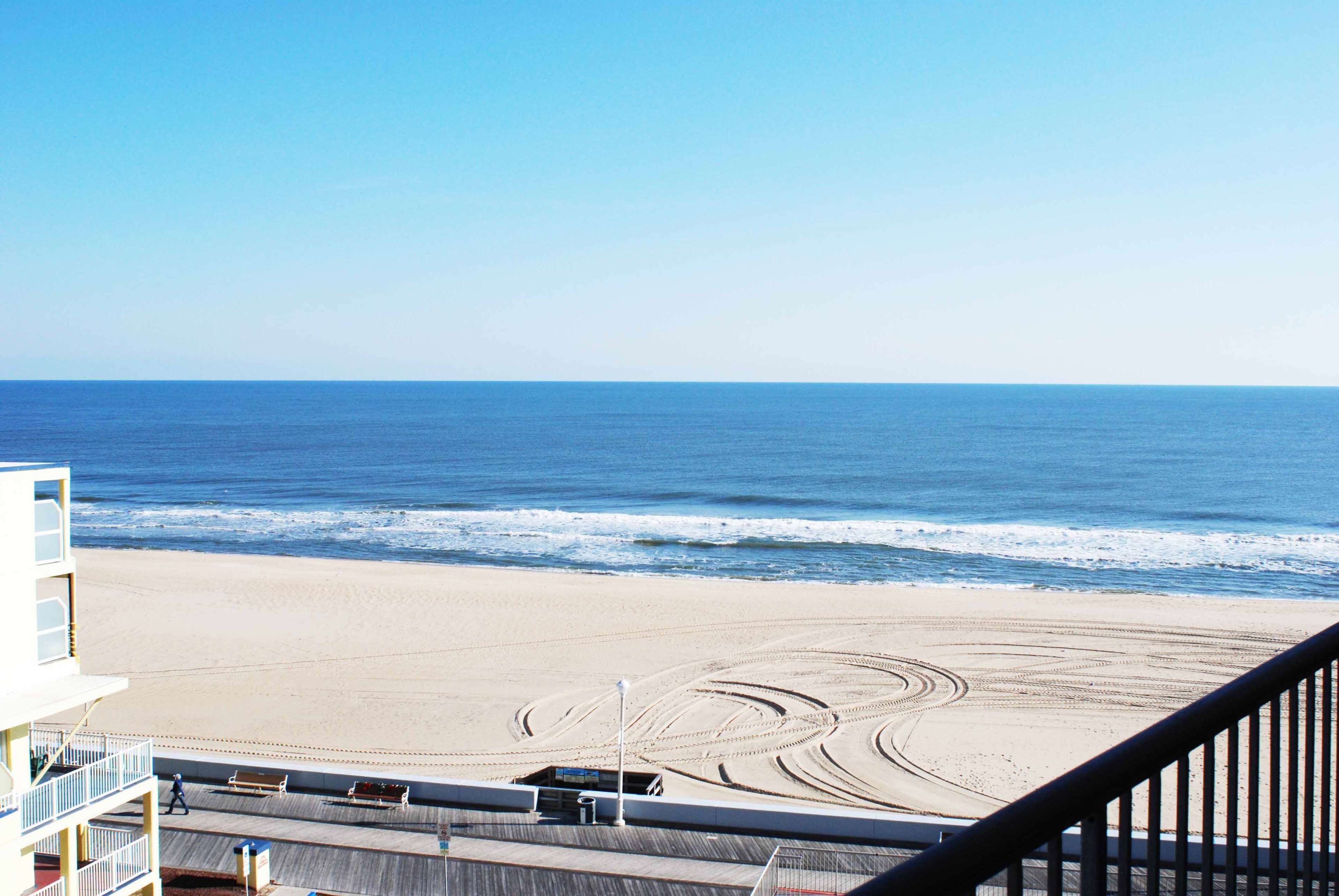 A beach view from a balcony with a wooden deck and a sandy beach in the foreground.