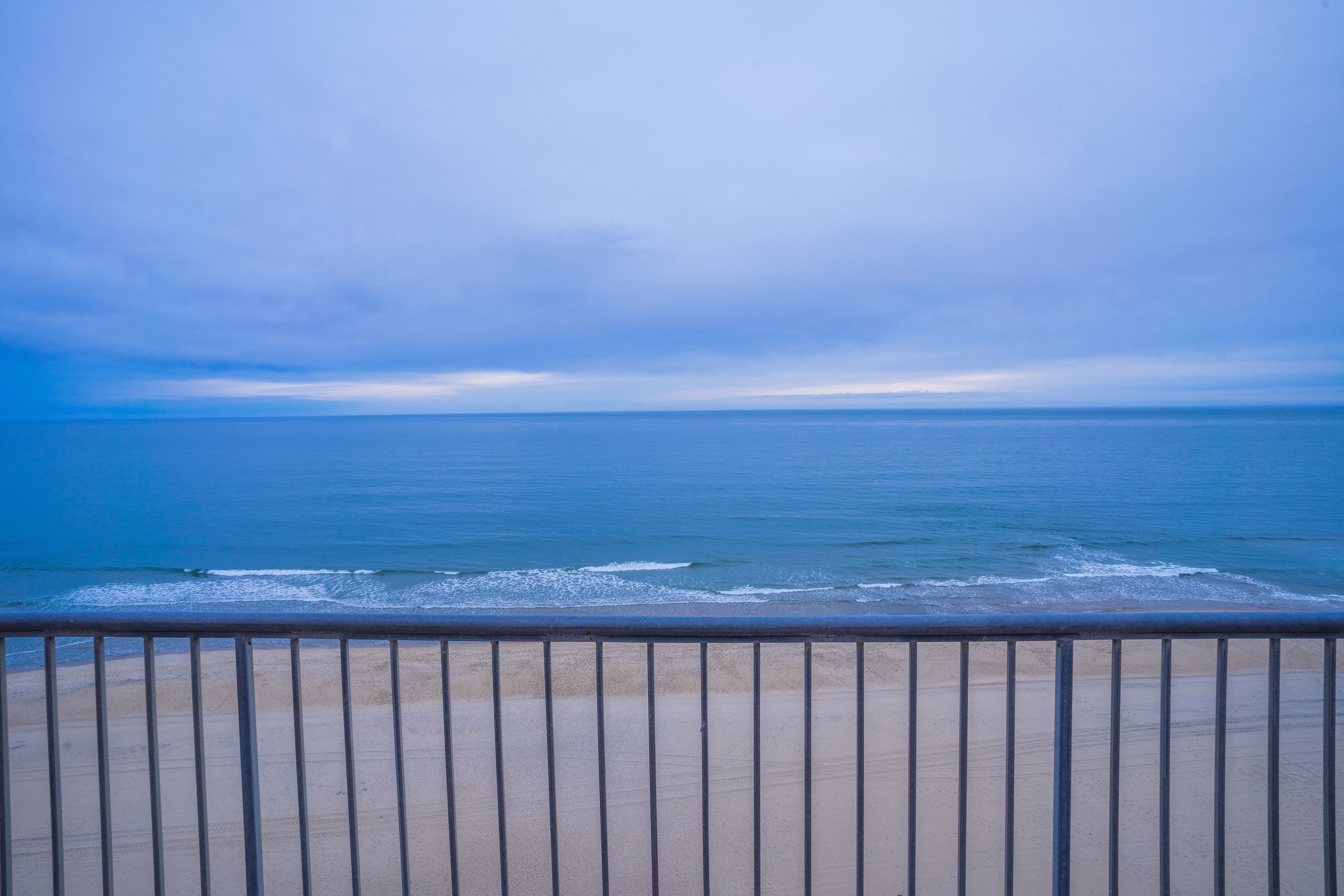 A beach view with a metal railing in the foreground.