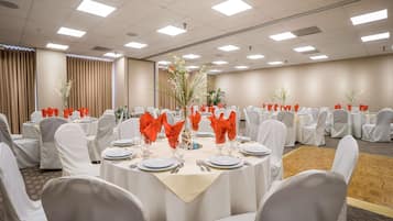 A conference room with round tables, white chairs, and red napkins.