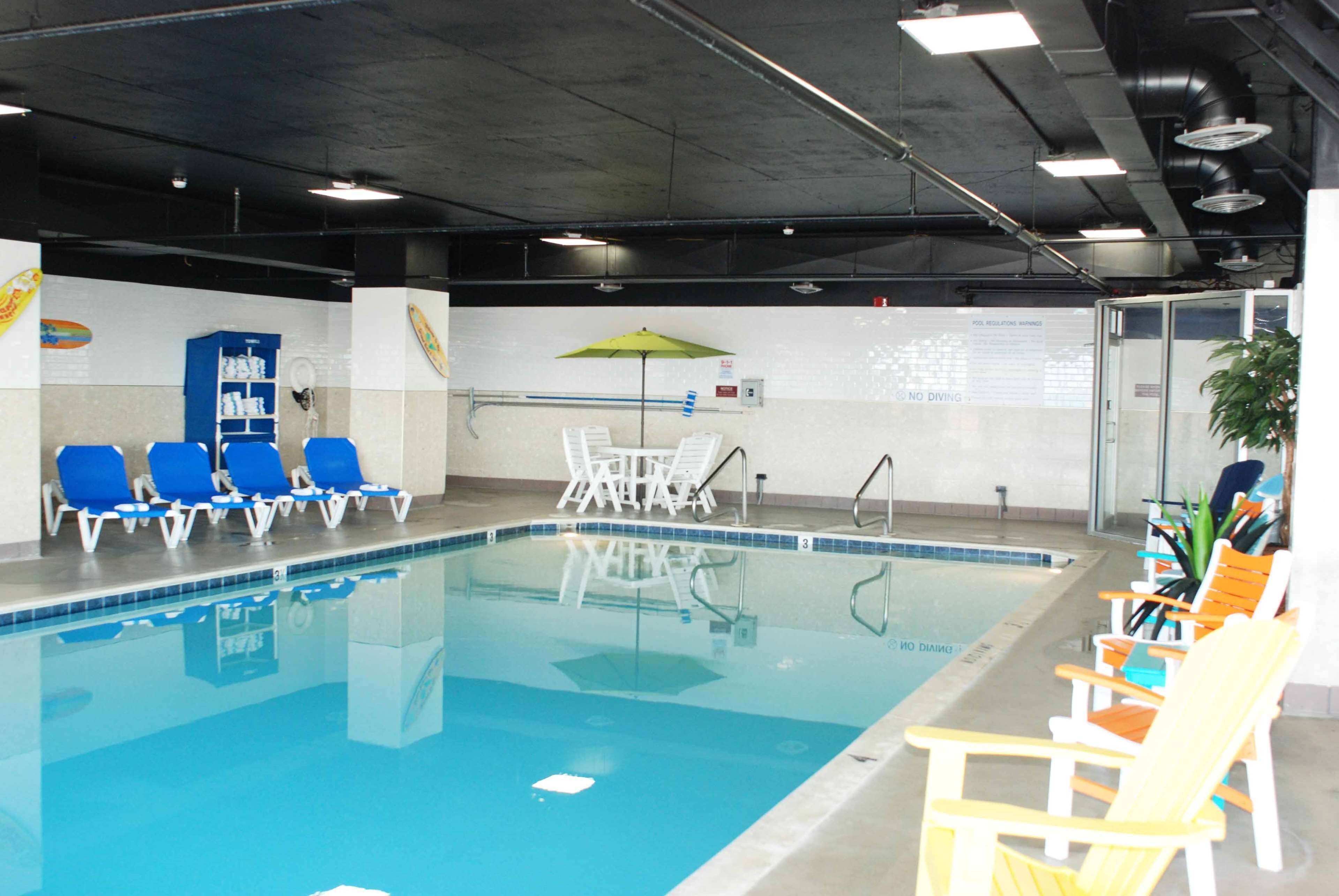 An indoor swimming pool with blue water, surrounded by white lounge chairs and a blue cabinet.