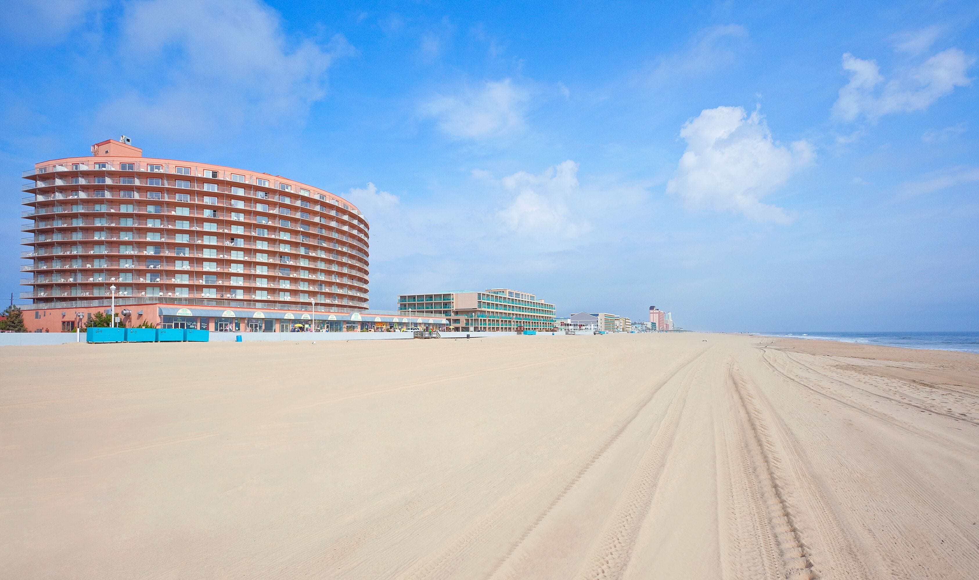 A beachfront hotel with a curved building, multiple balconies, and a sandy beach in the foreground.