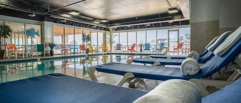 Zona de piscina con sillas de descanso y toallas, ventanas amplias con vistas y plantas de interior.