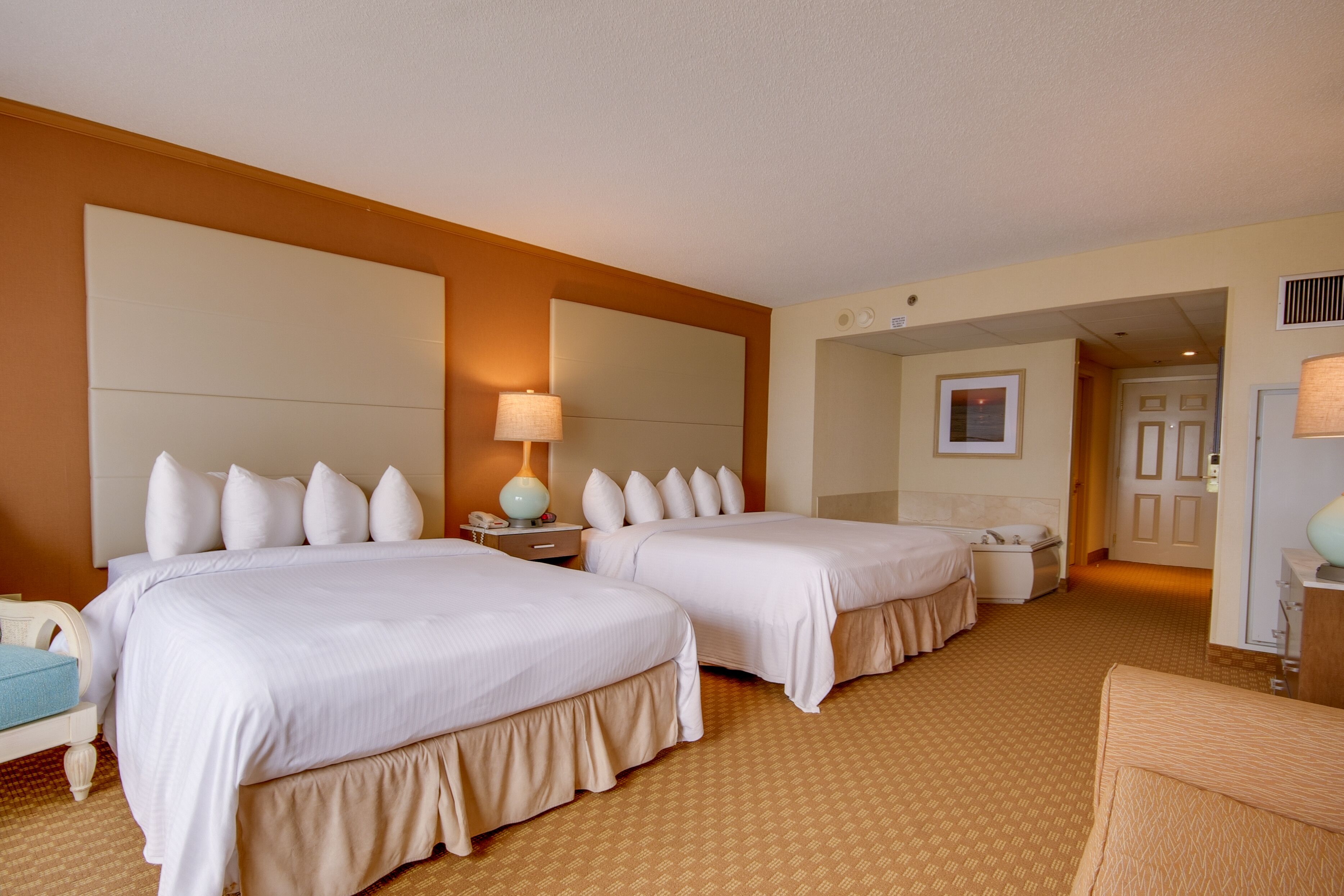 A hotel room with two beds, a nightstand, a lamp, and a door leading to another room.