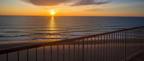 A sunset over the ocean with a metal railing in the foreground.