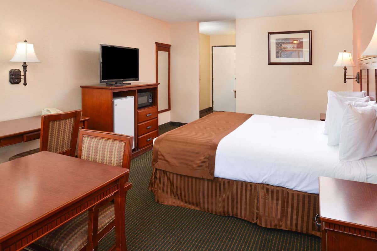 A hotel room with a bed, a desk, a television, a microwave, and a dresser.
