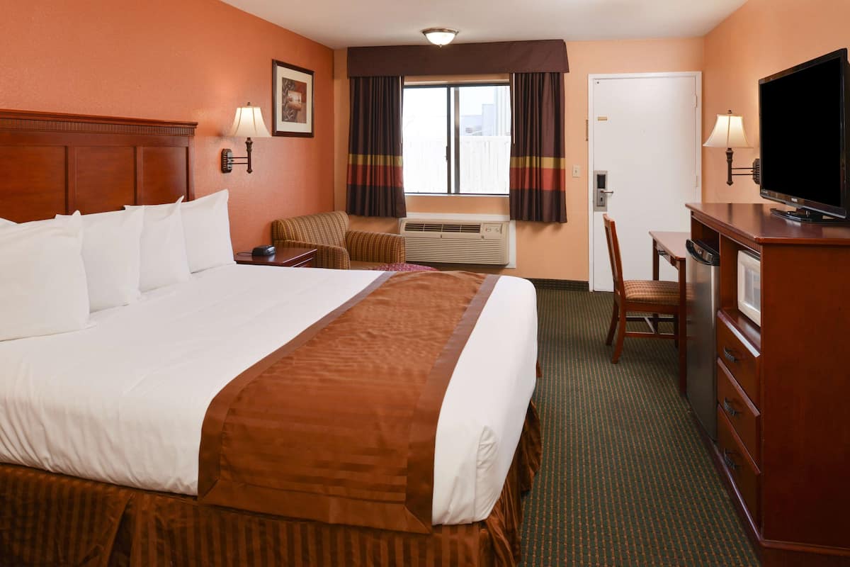 A hotel room with a large bed, a desk with a chair, a television, and an air conditioning unit.
