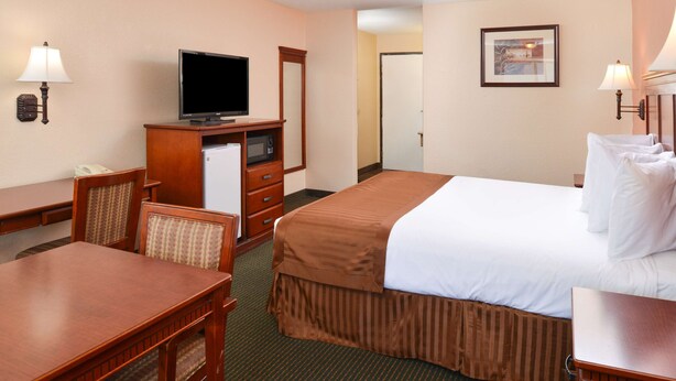 A hotel room with a bed, a desk, a television, a refrigerator, and a chair. - Americas Best Value Inn & Suites Bakersfield E (Bakersfield)