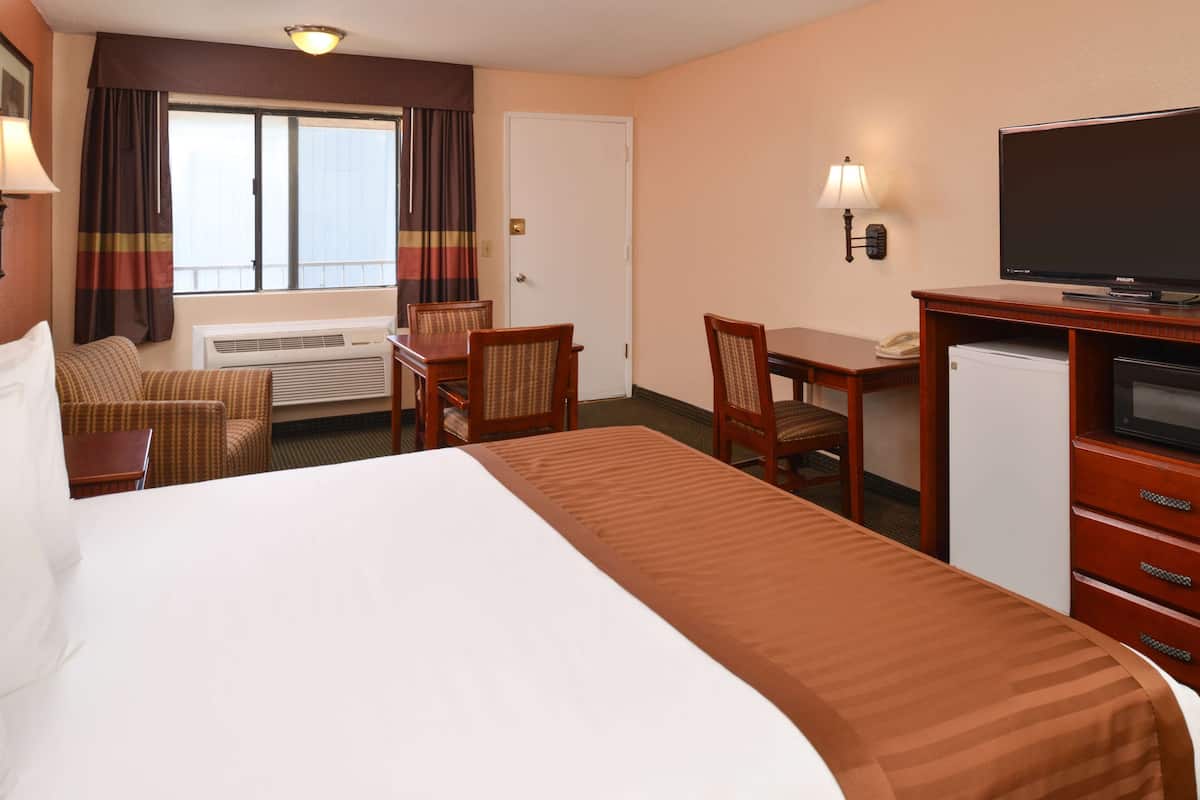 A hotel room with a large bed, a desk with a television, a chair, and a small refrigerator.