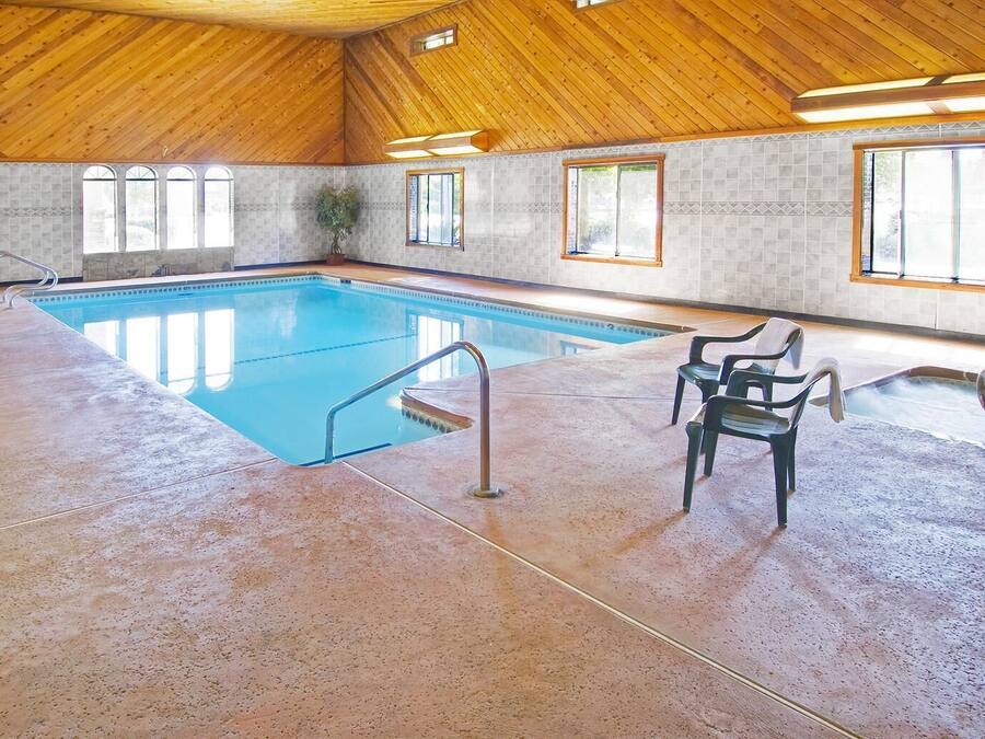 Una piscina interior amb sostre de fusta, parets enrajolades i un sòl de formigó.