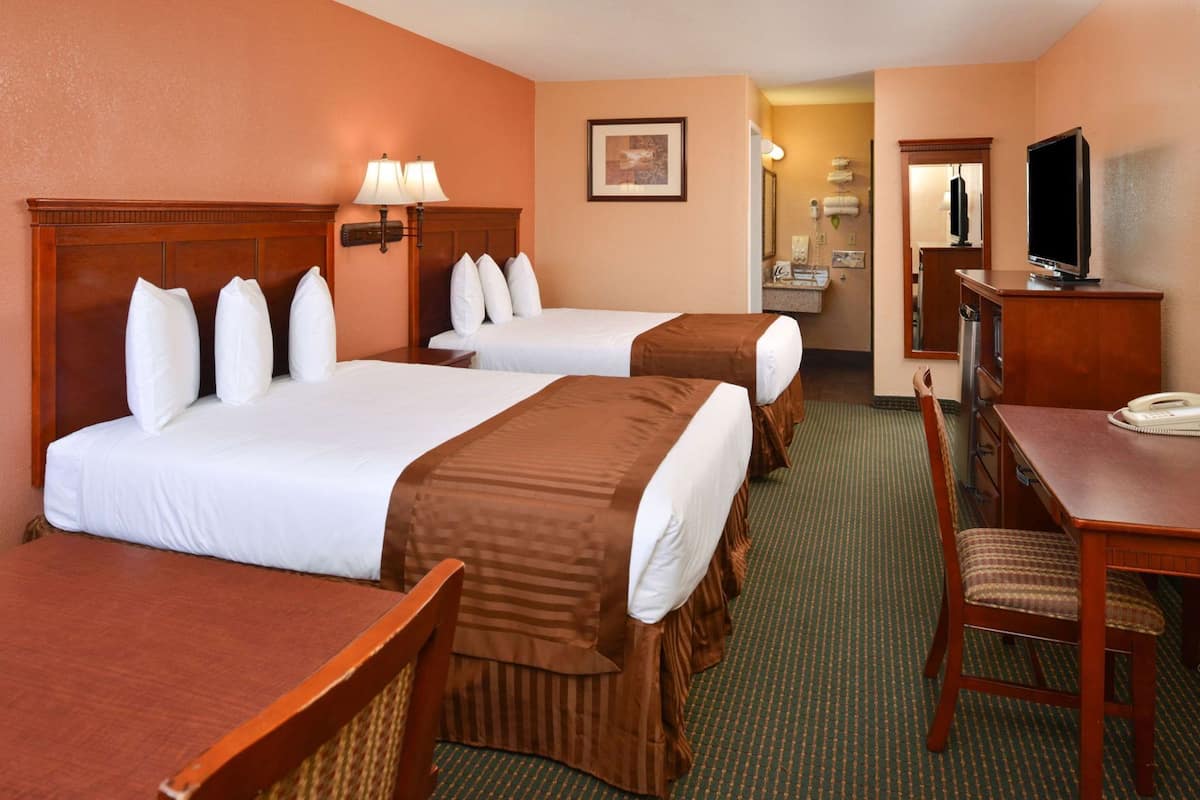A hotel room with two beds, a desk, a chair, a television, and a bathroom visible through an open door.