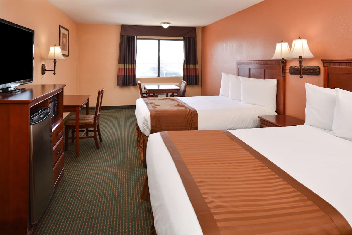 A hotel room with two beds, a desk, a television, and a window with curtains.