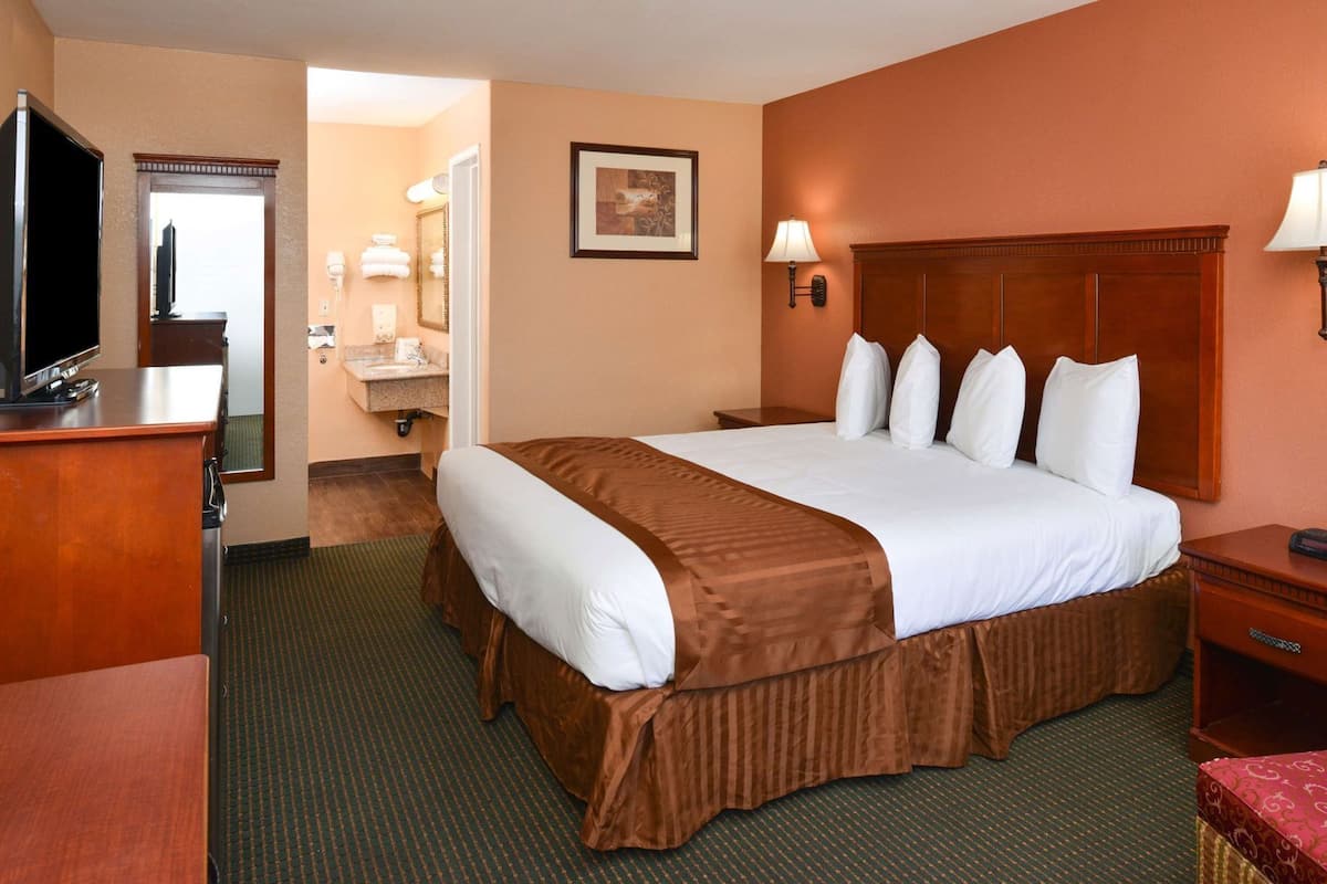 A hotel room with a large bed, a television, a desk, and a bathroom visible through an open door.