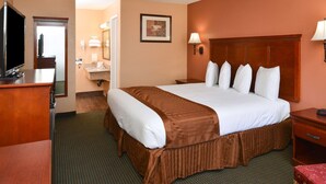 A hotel room with a large bed, a desk with a flat-screen TV, a bathroom with a sink and mirror, and a framed picture on the wall.
