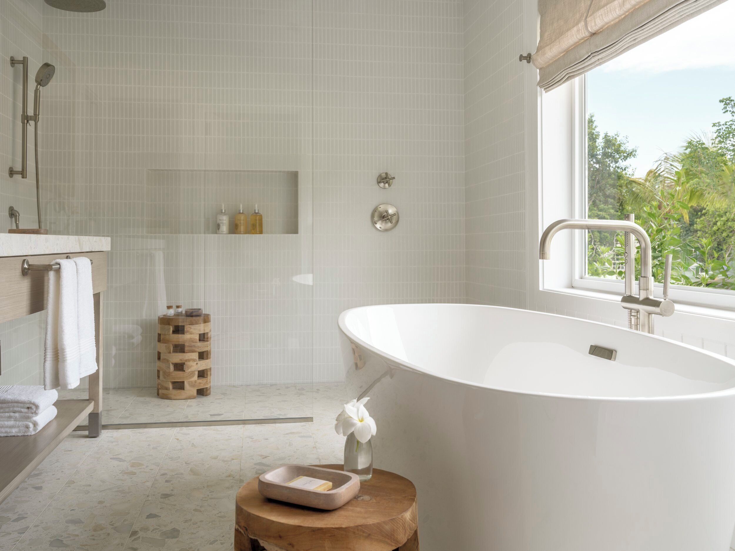 Un baño moderno con una bañera independiente, un taburete de madera y una ventana con vistas a la vegetación.