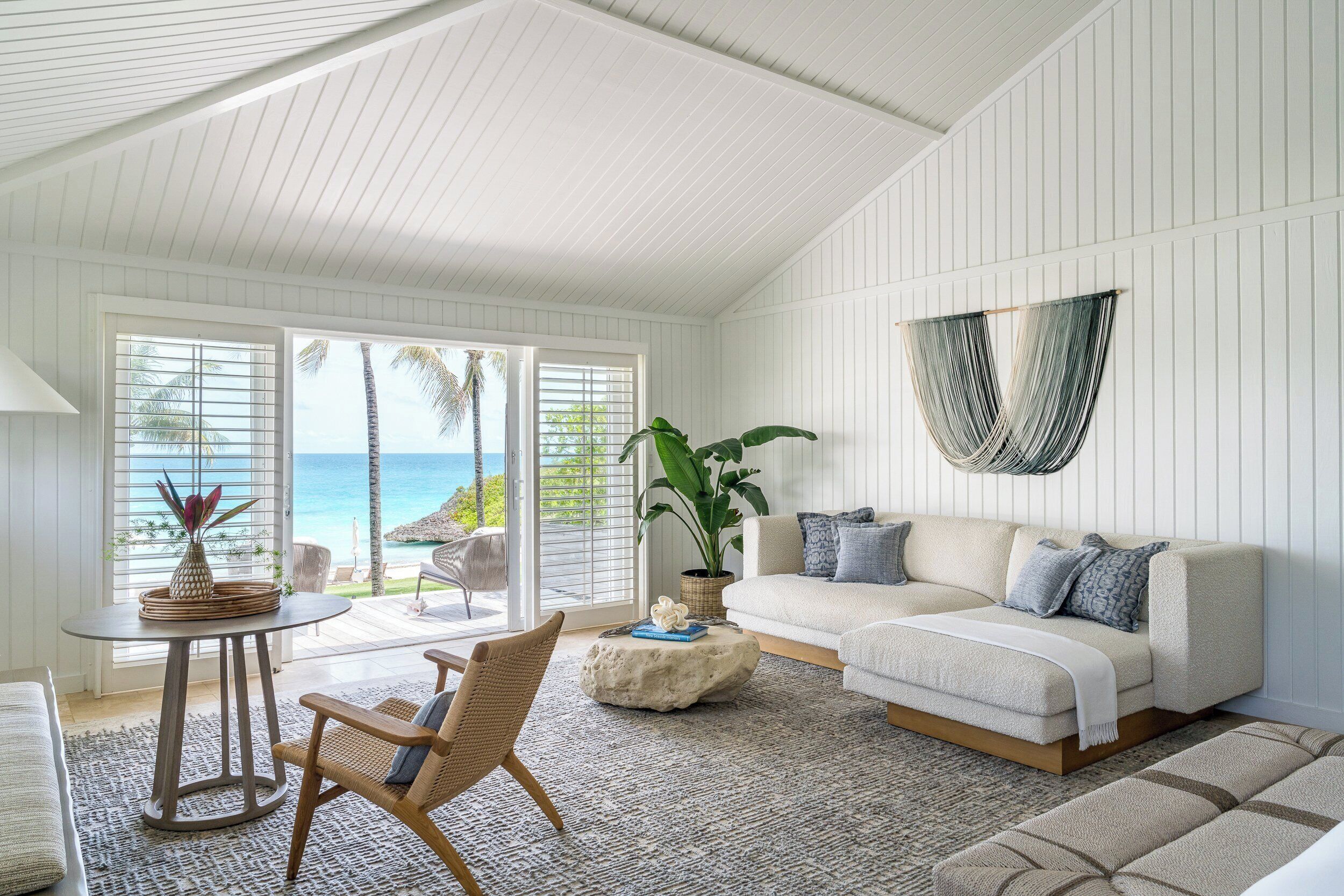 Ein geräumiges Wohnzimmer mit großem Fenster zum Meer, einem gemütlichen Sofa, einem runden Couchtisch und einem bequemen Sessel.
