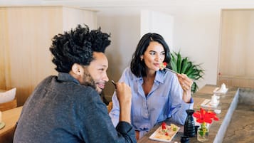 Una pareja cenando en una mesa con diversos platos, un jarrón con flores y una tetera.