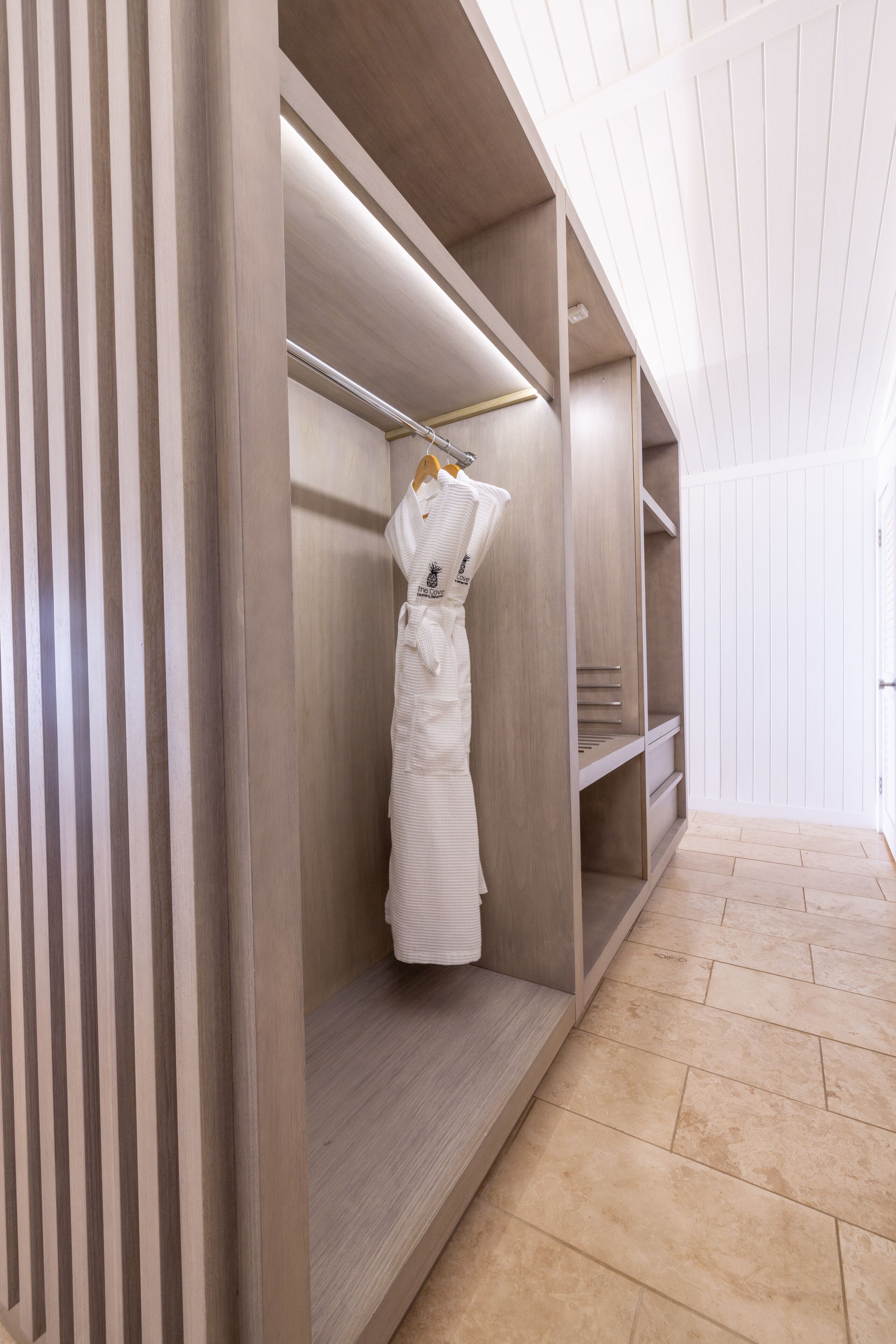 A modern, well-lit walk-in closet with wooden shelving and a hanging robe rack.