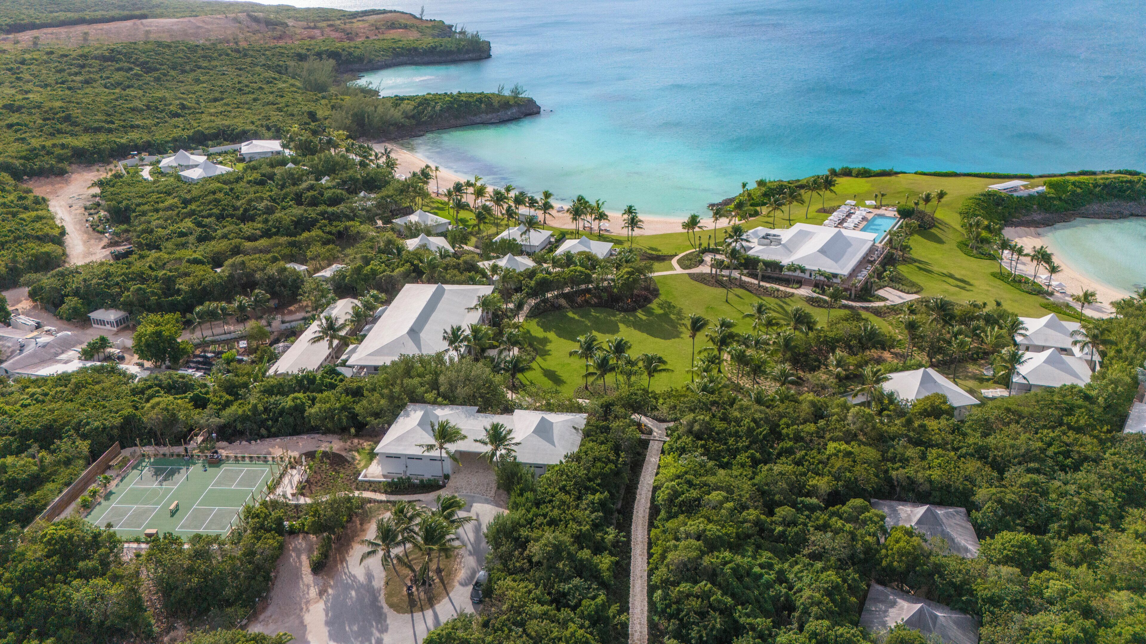 An aerial view of a resort with multiple buildings, a tennis court, and a beach area.