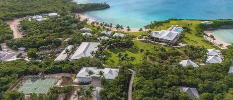 An aerial view of a resort with multiple buildings, a tennis court, and a beach area.