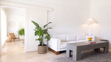 Una sala de estar moderna con un sofá blanco, una mesa de centro, una lámpara de pie, una planta en maceta y una silla de mimbre.
