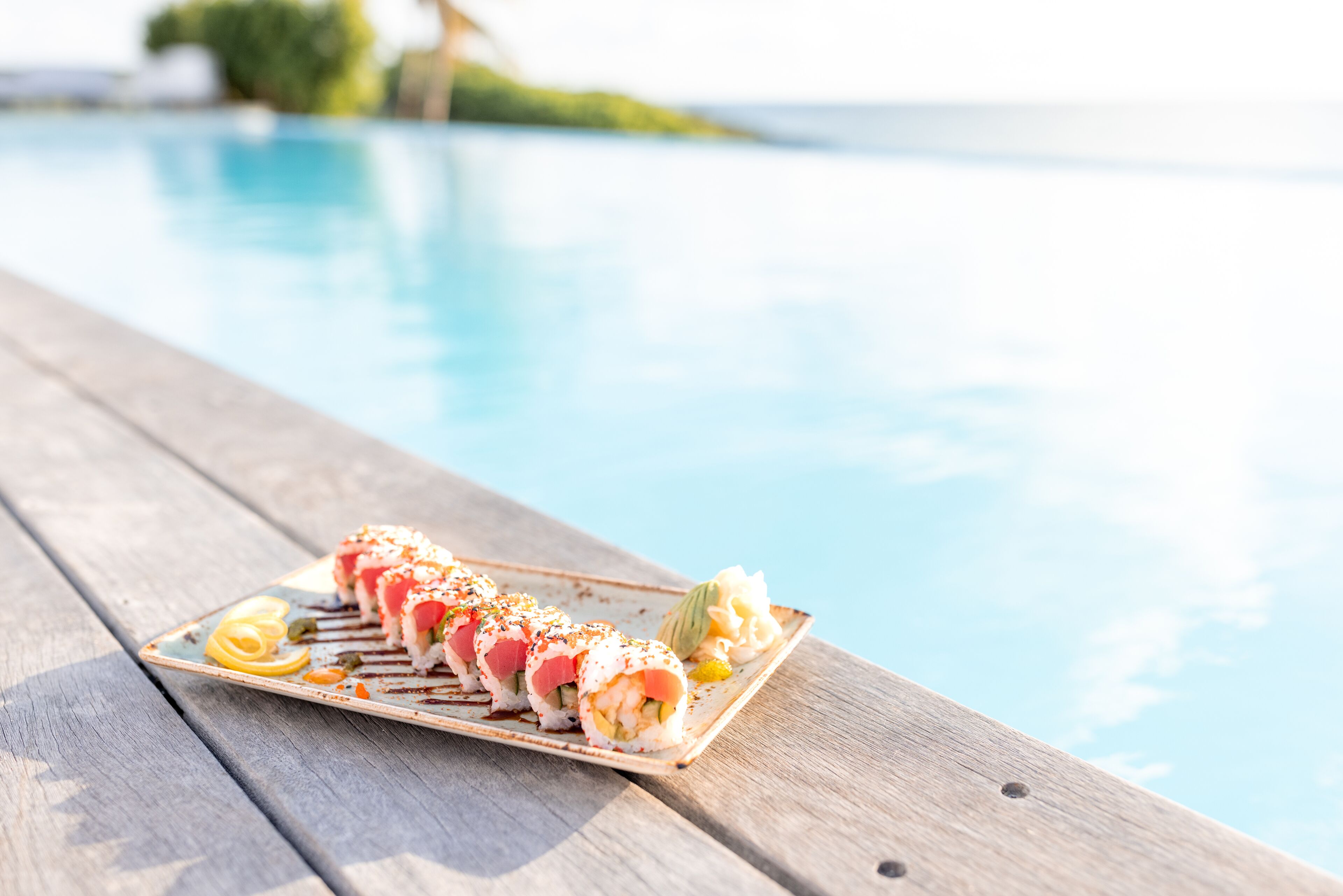 Eine Sushi-Platte auf einem Holztisch am Poolrand.