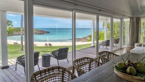 A covered outdoor area with a wooden deck, wicker chairs, and a table with a fruit bowl. - The Cove Eleuthera (Gregory Town)
