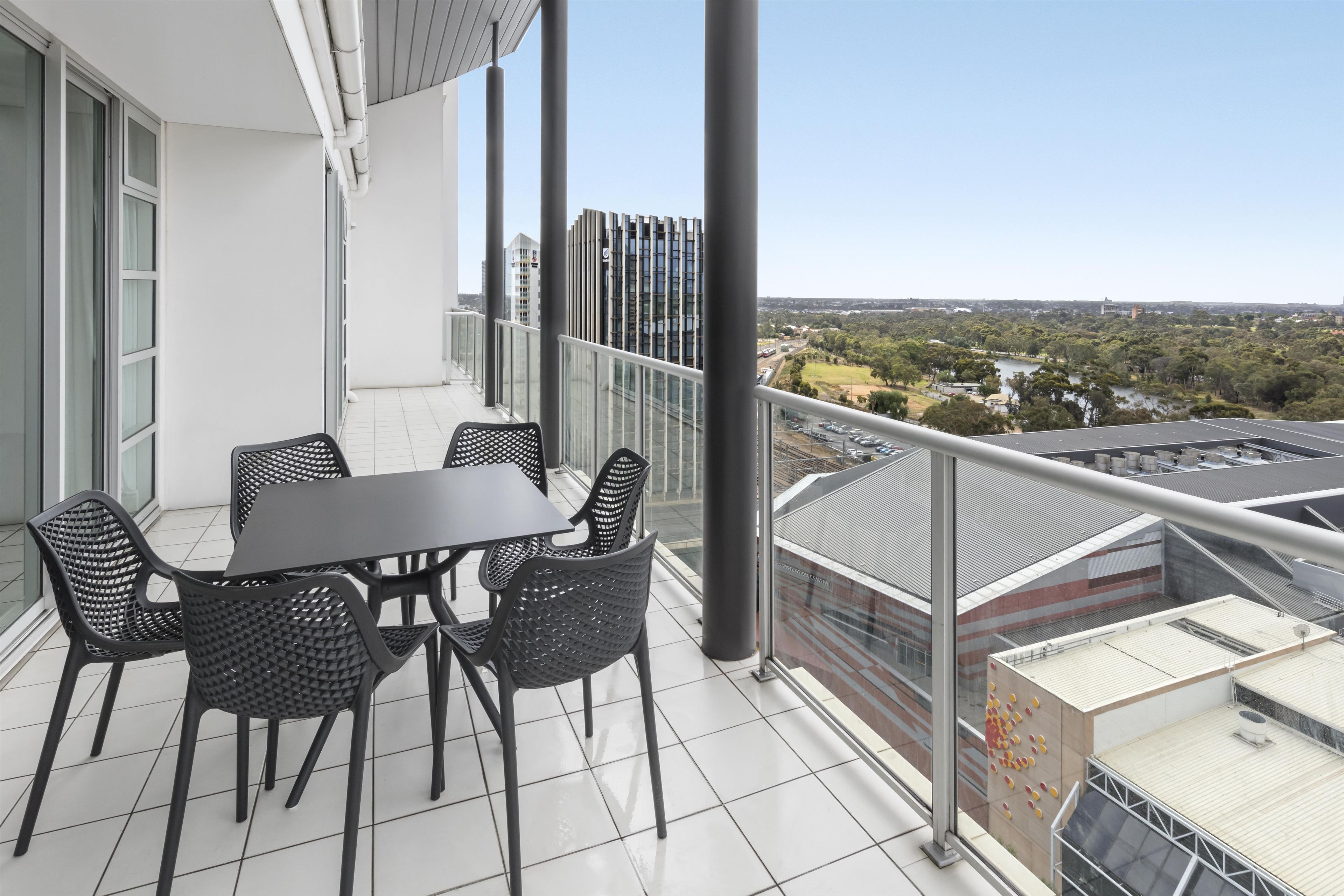 Un balcon avec une table et des chaises, d’où l’on peut admirer une vue sur la ville et sur une rivière.