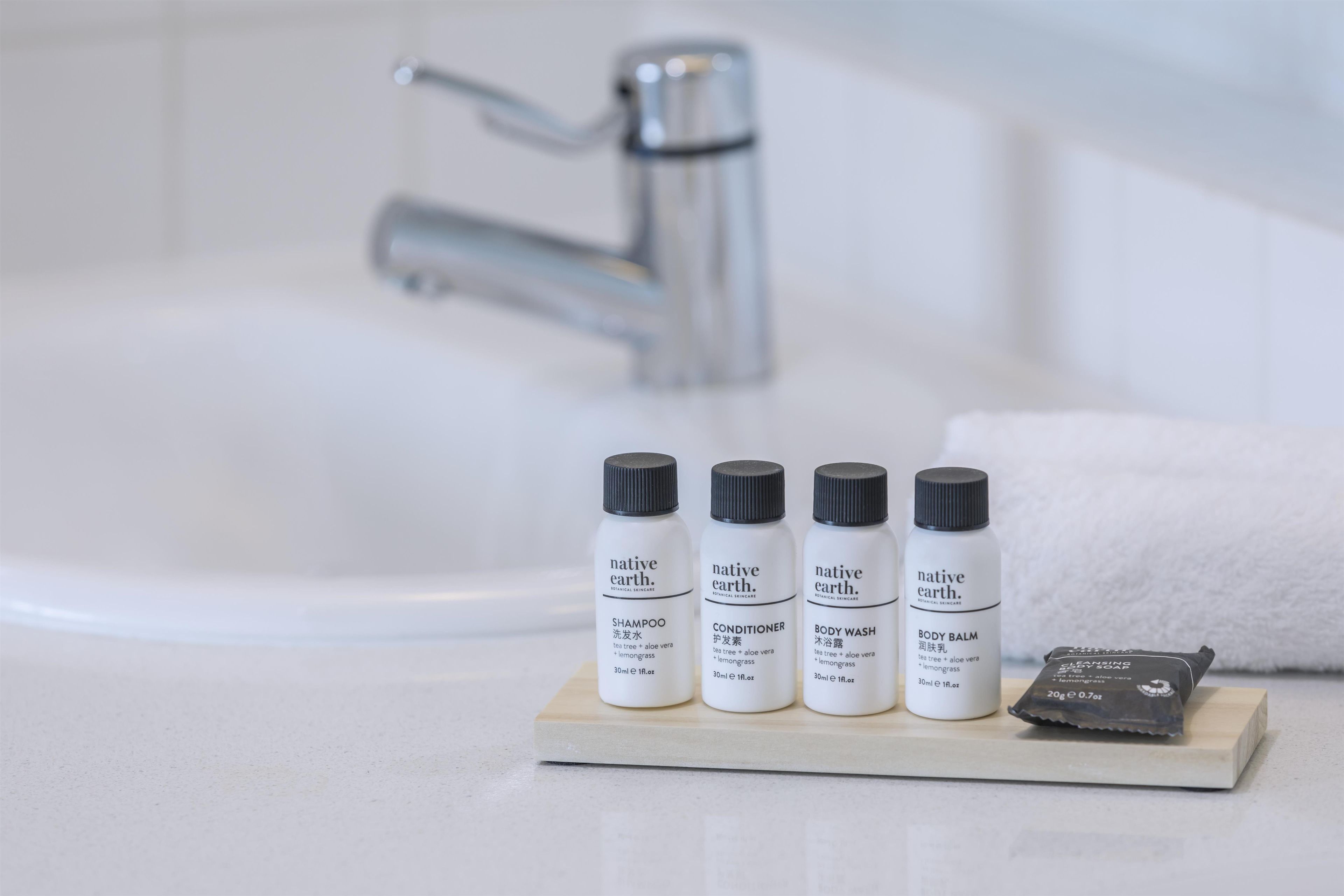 A bathroom with a white sink, four bottles of native earth skincare products, and a bar of soap on a wooden tray.