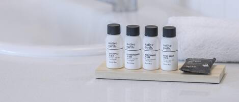 A bathroom with a white sink, four bottles of native earth skincare products, and a bar of soap on a wooden tray.