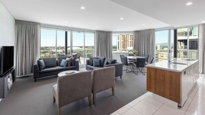 Una sala de estar moderna con un sofá, sillones, una mesa de centro y una cocina con fregadero y armarios.
